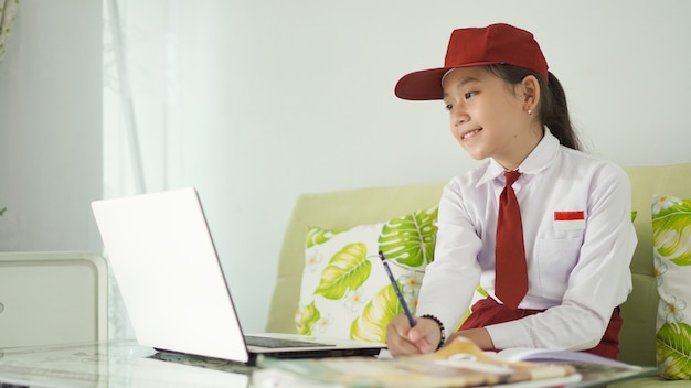 Menina asiática do ensino fundamental estudando online em casa fazendo anotações no laptop