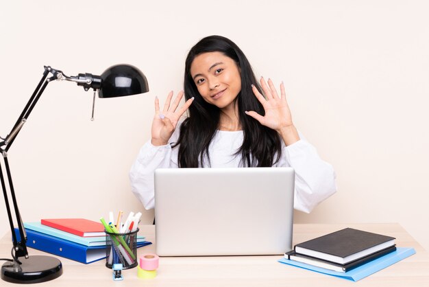 Menina asiática do estudante em um local de trabalho com um laptop isolado no bege