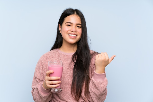 Menina asiática do jovem adolescente com milk-shake de morango apontando para o lado para apresentar um produto