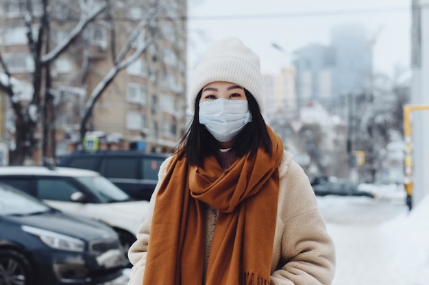 Menina asiática do transeunte em uma máscara médica protetora ao ar livre. Uma mulher na rua no inverno protege o trato respiratório da epidemia de coronavírus