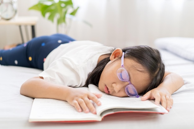 Menina asiática dorme cansada de ler um livro na cama