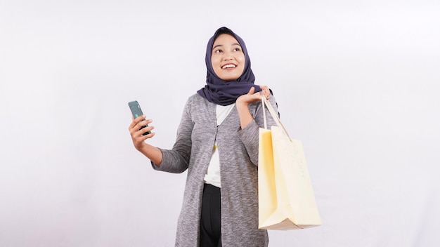 Menina asiática e sacola de compras usando smartphone e cartão de débito isolado no fundo branco