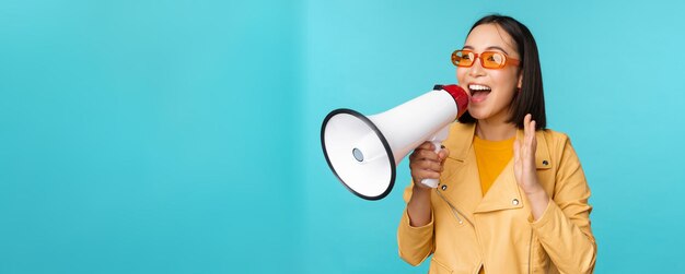 Menina asiática elegante fazendo anúncio no megafone gritando com viva-voz e sorrindo convidando