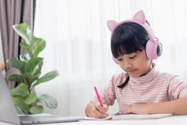 Menina asiática em fones de ouvido tem aula distante de videochamada com professor usando laptop estudo on-line no conceito de ensino doméstico de computador