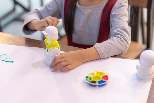 Menina asiática está pintando uma boneca na sala de aula de arte, para o conceito de criatividade