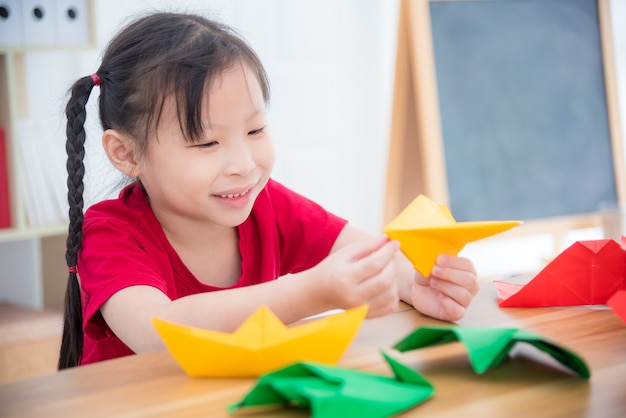 Menina asiática fazendo avião de papel de dobradura de papel na escola.