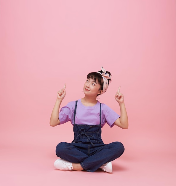 Menina asiática feliz apontando os dedos para cima no fundo rosa com espaço de cópia