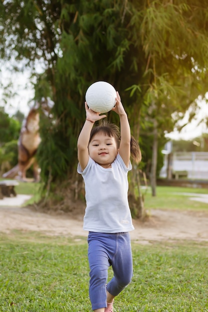 Menina asiática feliz correndo ou pulando e brincando no parque ou no campo do jardim. Ela sorrindo e rindo