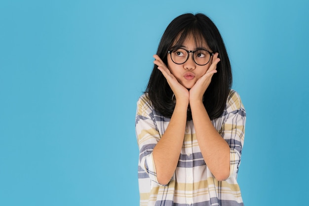 Menina asiática feliz em pé com óculos em fundo azul