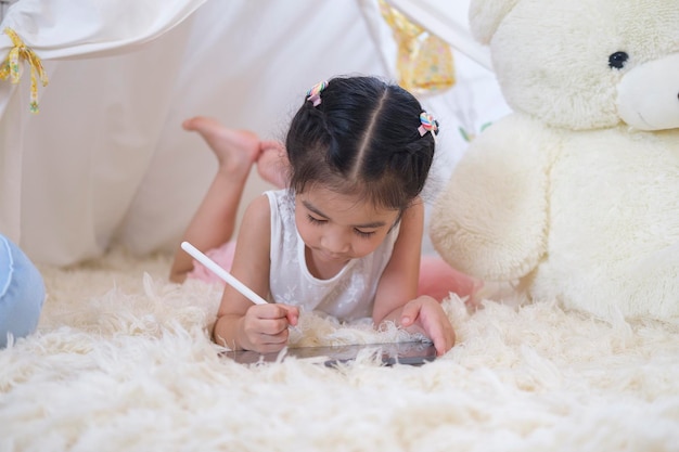 Menina asiática feliz escrevendo em tablet inteligente em casa