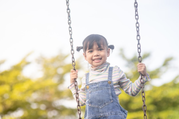 Menina asiática feliz jogando swing ao ar livre no parque