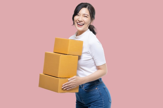 Menina asiática feliz segurando caixas de pacotes isoladas no fundo da tela rosa correio de entrega e conceito de serviço de transporte
