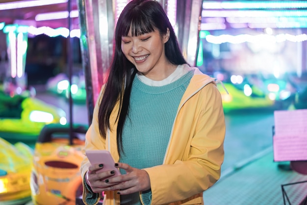 Menina asiática feliz usando smartphone em parque de diversões