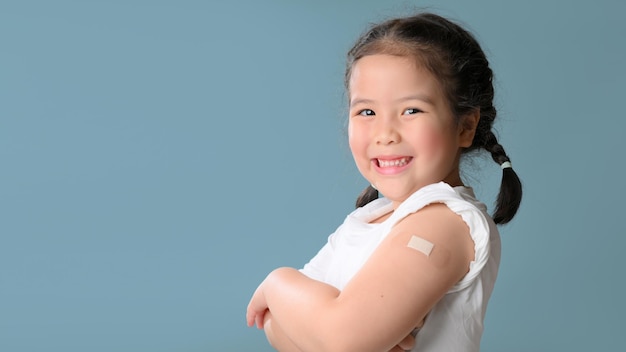 Foto menina asiática feliz vacinada mostrando o braço com atadura de gesso após injeção de vacina