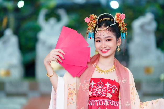 Menina asiática feliz vestindo fantasias chinesas segurando decoração de envelopes vermelhos para o festival do ano novo chinês celebrando a cultura da china no santuário chinês Lugares públicos na Tailândia