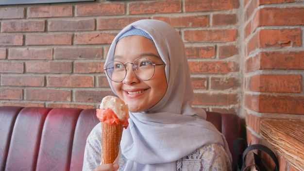 Menina asiática hijab enquanto desfruta de sorvete de gelato