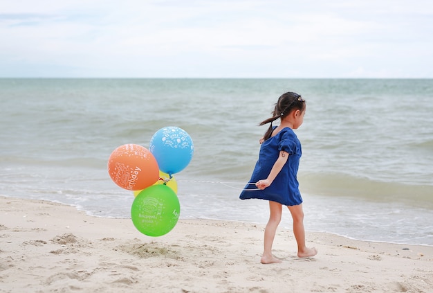 Menina asiática jogando balões na praia