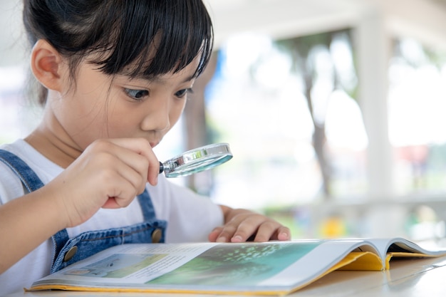 Menina asiática lendo os livros na mesa com uma lupa