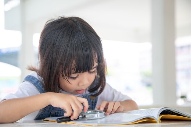 Menina asiática lendo os livros na mesa com uma lupa