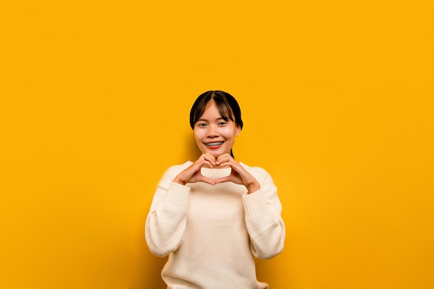 Menina asiática Linda vestindo um vestido casual branco em um fundo amarelo Comemore a vitória com um sorriso feliz e a expressão do vencedor com uma expressão feliz de mão erguida