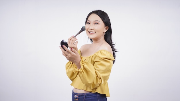 Menina asiática maquiada aplicando blush na bochecha isolada no fundo branco