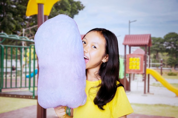 Menina asiática mordendo um algodão doce no playground