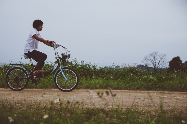 Menina asiática nova com a bicicleta do vintage na paisagem da natureza do campo.