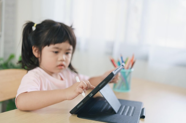 Menina asiática olhando e tocando na tela branca na tela do tablet atentamente conceito de crianças superestimuladas Muito tempo de tela Linda garota assistindo vídeos enquanto tv conceito de vício em Internet