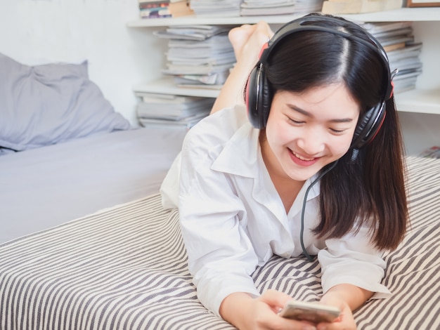 Menina asiática ouvindo música em fones de ouvido na cama