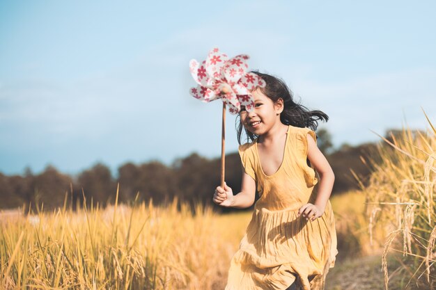 Foto menina asiática pequena asiática bonito que joga com turbina de vento e que funciona no campo de milho no tom de cor do vintage