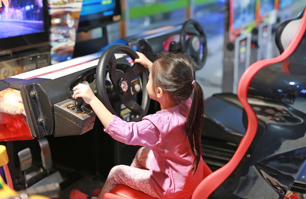 Menina asiática pequena da criança que joga o carro de competência da arcada do jogo.