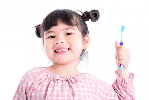 Menina asiática pequena segurando a escova de dentes e sorrisos sobre fundo branco