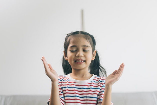 Menina asiática rezando no sofá na sala de estar