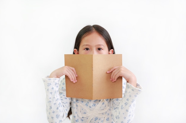 Menina asiática segurando a capa de um livro marrom e escondendo a boca e o nariz olhando para a câmera sobre o branco
