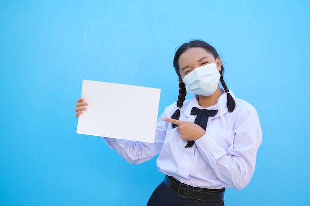 Menina asiática segurando um quadro branco sobre fundo azul. Aluna da escola