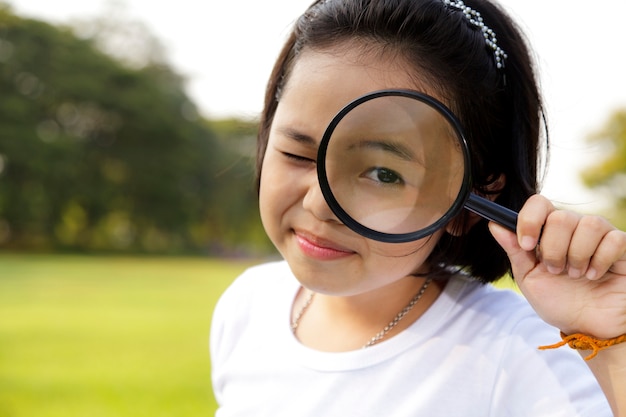 Menina asiática segurando uma lupa no exterior