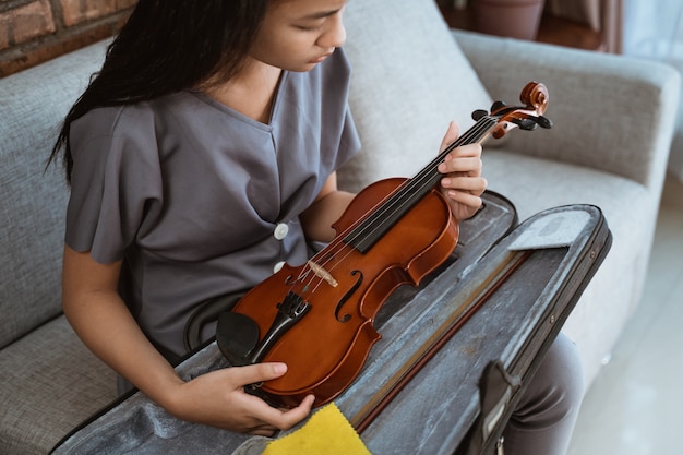 Menina asiática sentada no sofá segurando um violino