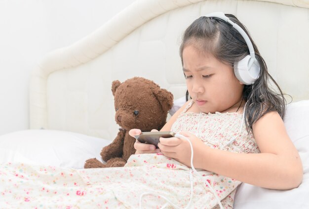 Menina asiática séria que joga no telefone esperto