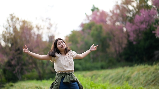 Menina asiática sorri maliciosamente e se vira para a câmera durante um passeio pela natureza. Ela abre os braços.