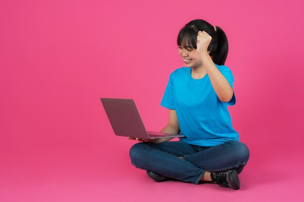 Menina asiática sorridente feliz usando laptop em fundo rosa