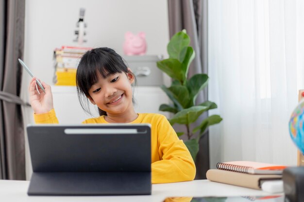 Menina asiática tendo aula on-line e feliz pelo conceito de pandemia de coranavírus de quarentena escolar em casa