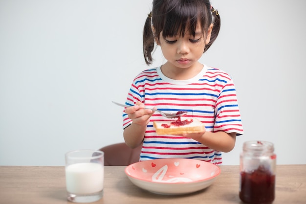 Menina asiática tomando café da manhã com pão e geléia com um copo de leite