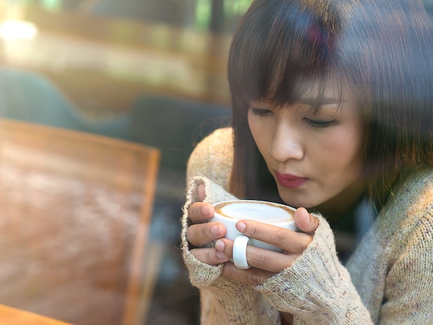 Menina asiática tomando café quente no café para relaxar na manhã de domingo