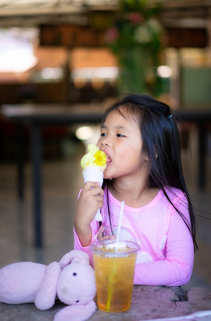 Menina asiática tomando um sorvete com bebida e boneca interior