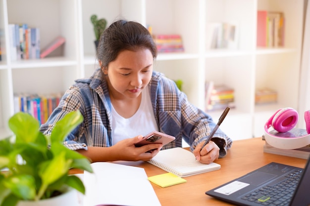 Menina asiática usando estudo de telefone inteligente em casa