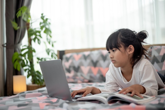 Menina asiática usando um laptop enquanto estava deitado na cama