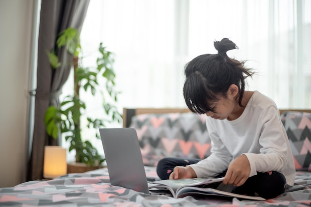 Menina asiática usando um laptop enquanto estava deitado na cama