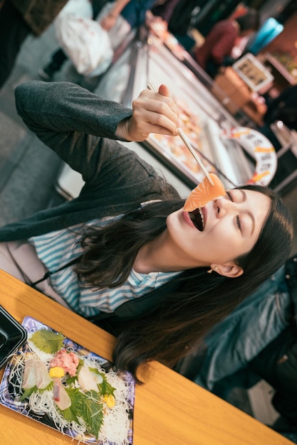 menina asiática viajando animado comendo peixe cru fresco no mercado kuromon. estilo de vida de comida local japonesa em osaka. jovem alegremente tentando sashimi.