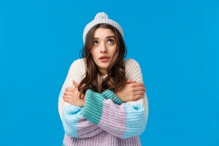 Foto menina assistindo em flocos de neve, olhando para cima e tremendo de frio em pé no chapéu do inverno, camisola