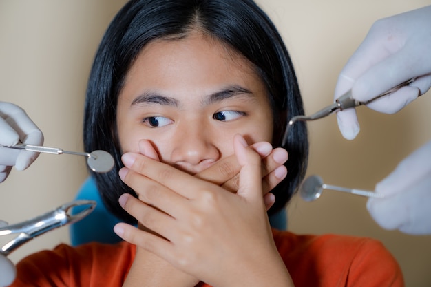 Menina assustada por dentistas cobre a boca no consultório do dentista